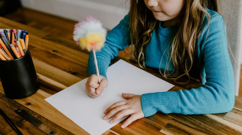 Ein Mädchen malt an einem Tisch auf ein Blatt Papier.