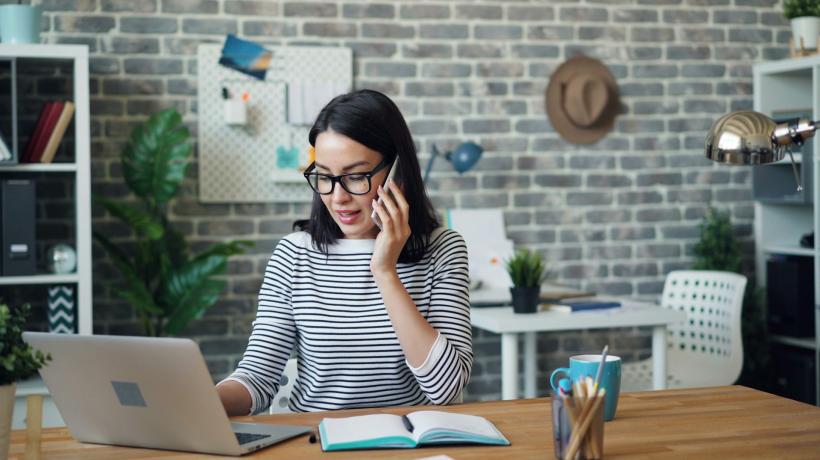 Foto: Vitaly Gariev – unsplash.com Eine junge Frau sitzt in Ihrem Büro, telefoniert mit dem Handy und sitzt am Laptop