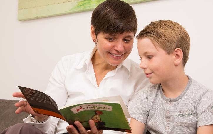 Therapeutin schaut gemeinsam mit einem Jungen ein Bilderbuch an.